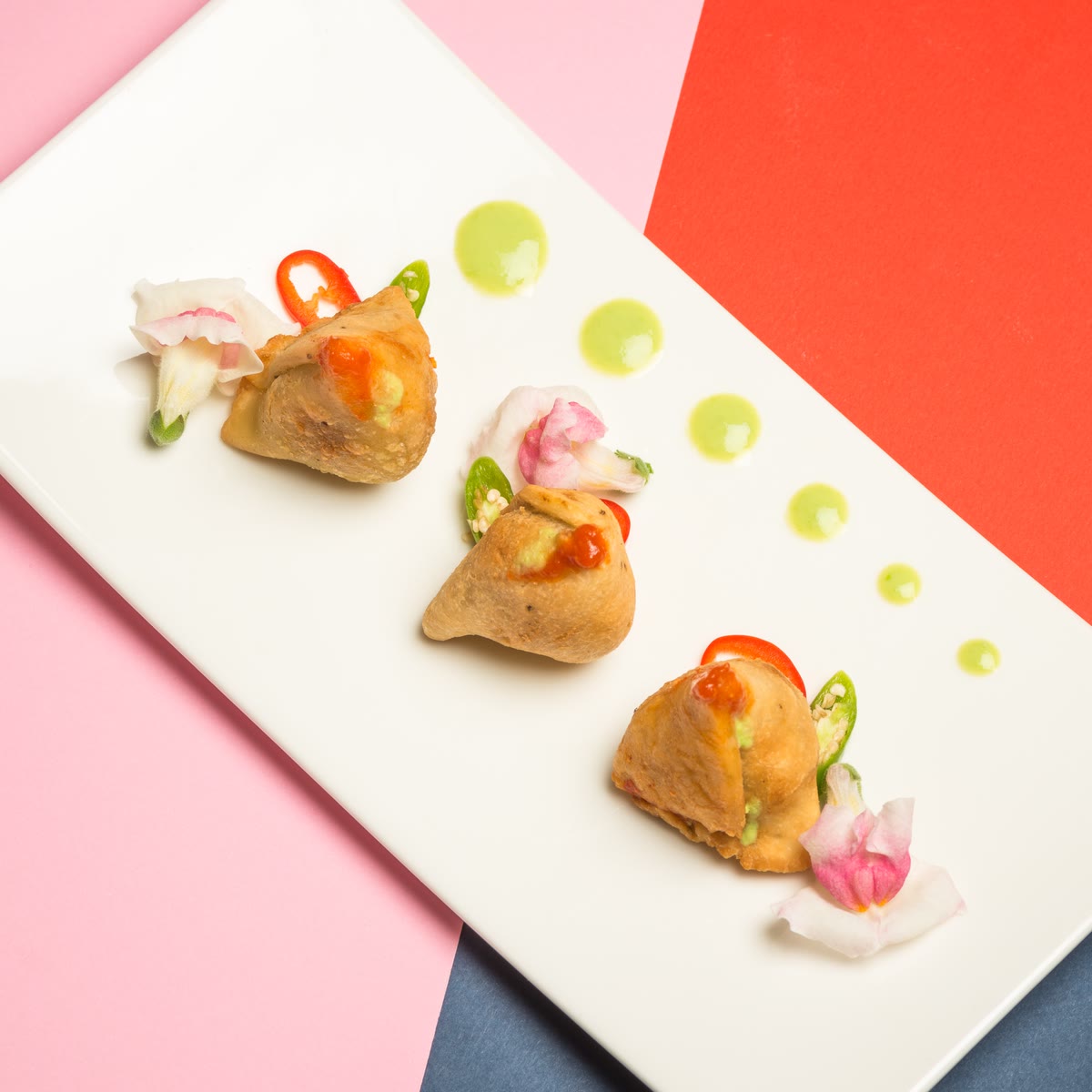Tre samosa su un piatto bianco con gocce di chutney verde