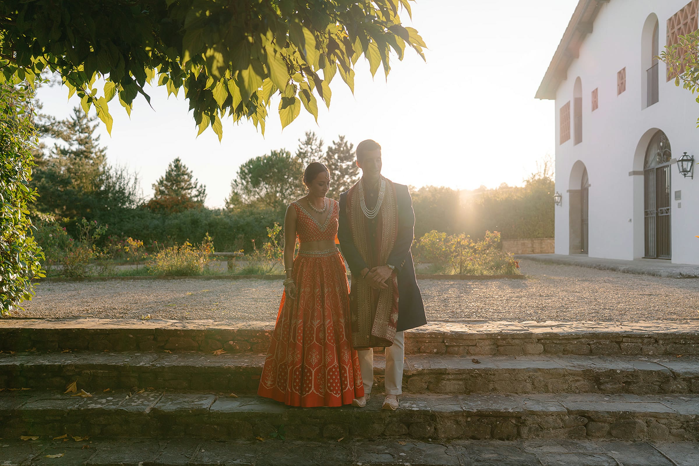 Gli sposi sui gradini di pietra di Viesca, controluce al tramonto, lei in un lehenga arancio